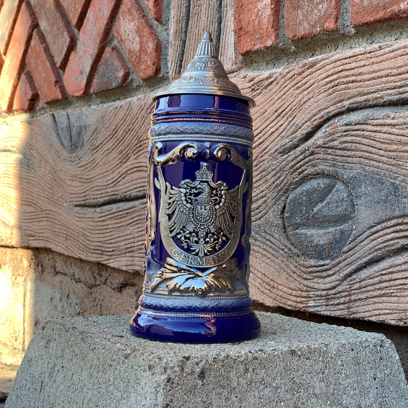 Ceramic Beer Mugs make every German beer taste better! To top off good German beer, this .7L (features elegant raised ceramic relief design around the medallion area) ceramic mug beer stein is accented with a metal medallion which features a variation of "The Reichsadler" (Imperial Eagle) Deutschland Eagle Coat of Arms Crest which is derived from the Roman eagle standard used by the Roman emperors and has been used through the ages since medieval times to contemporary German republics.